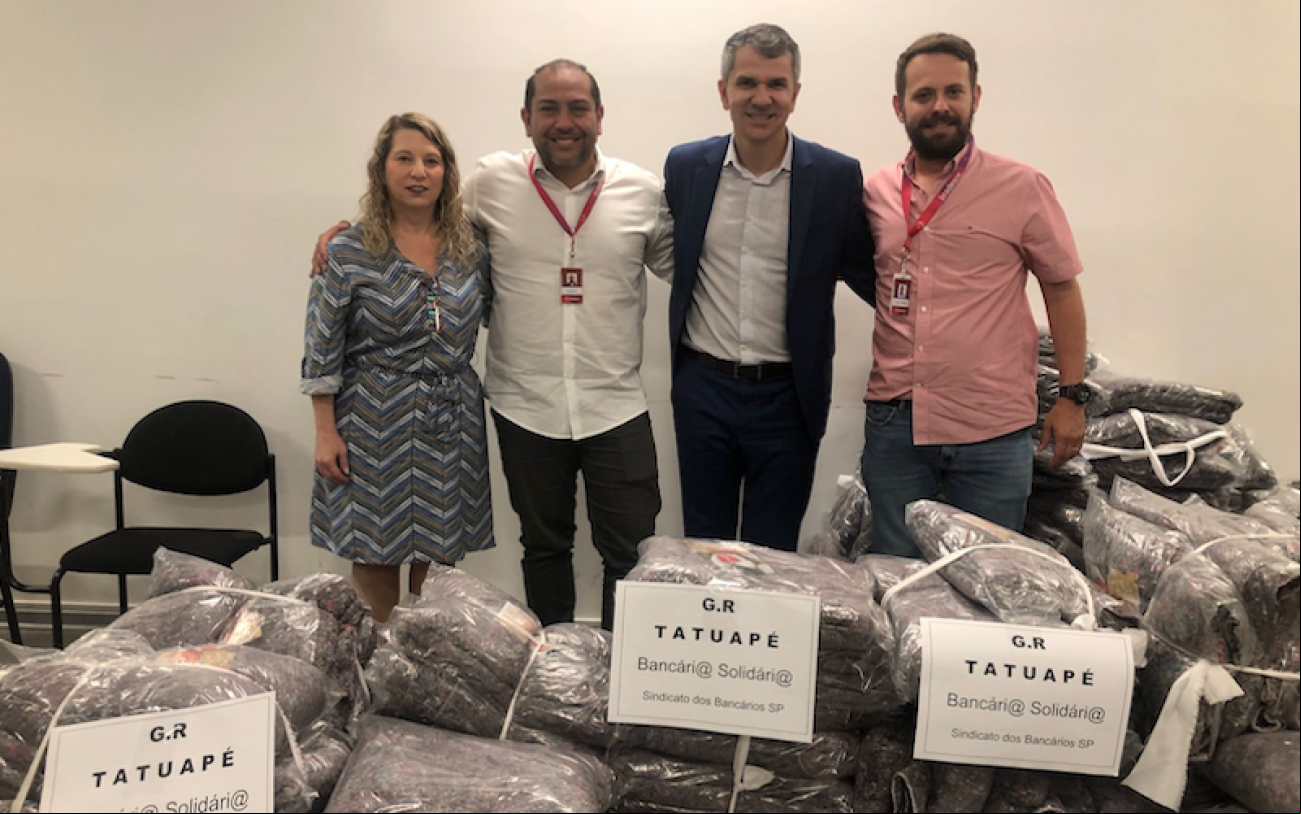 Foto: Seeb-SP Fotografia mostra os cobertores doados por bancários da G.R Tatuapé, do Bradesco, com dirigentes do Sindicato e bancários do Bradesco ao fundo