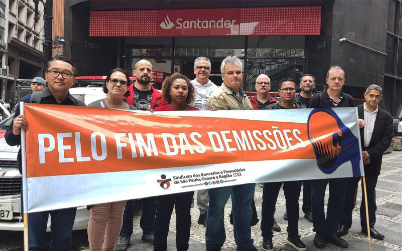 Imagem mostra dirigentes do Sindicato dos Bancários de São Paulo em frente ao Quarteirão de Investimentos, portando uma faixa onde se lê "pelo fim das demissões"