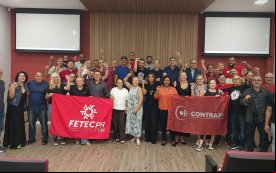 Fotografia mostra participantes da conferência de saúde com bandeiras vermelha de seus sindicatos nas mãos