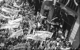 Imagem em preto e branco mostra eata de bancários durante a greve de 1989. A manifestação ocorre em uma rua no centro antigo de são paulo, em frente a uma agência do Itaú