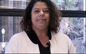 A foto mostra Ivone Silva, a presidenta do Sindicato dos Bancários de São Paulo, Osasco e região. Ela é uma mulher negra, com cabelos negros encaracolados, na altura dos ombros. Ela veste um terno rosa claro e uma camisa preta, e está sorrindo